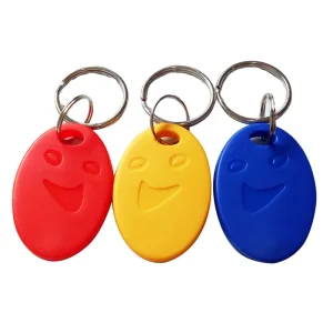 Three access control key fobs, each featuring a smiling face: one in red, one in yellow, and one in blue. Attached to metal key rings, these fobs add a quirky and joyful touch to your keys.