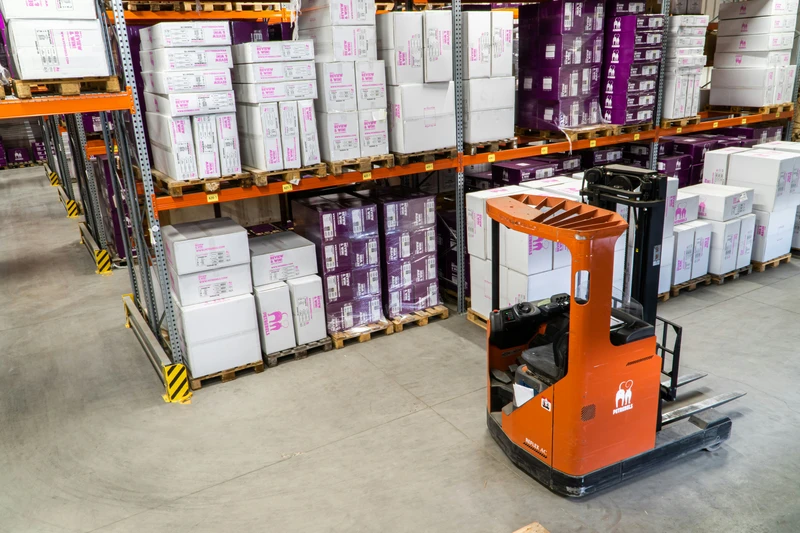 A warehouse with boxes stacked on metal shelves and an orange forklift in the foreground, showcasing modern inventory management technology, captured in photo-1616401784845-180882ba9ba8.